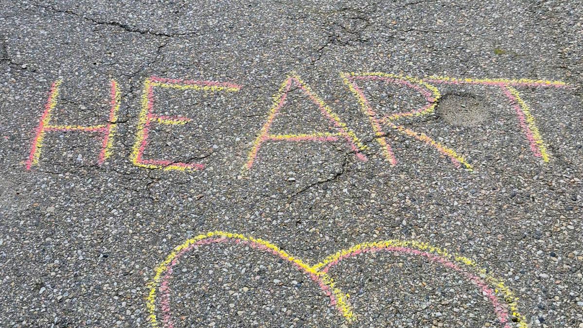 Yellow and pink chalk on pavement that reads, "Run with Heart" and shows a heart drawing below the text