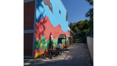 Bicycles attached to bike racks beside a colourful mural-painted brick wall