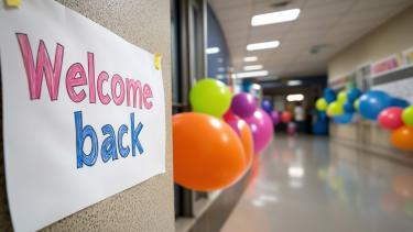 Welcome back to school! A handwritten "Welcome Back" poster on a hallway wall, with colorful balloons. The festive, celebratory of a school event or the first day back, with a blurred background of a school