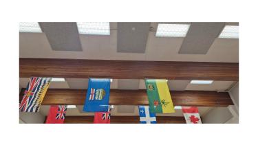 New acoustic tiles have been installed in the Hume Studio/Gymnasium! An image of a gymnasium ceiling showing fluorescent lights, flags hanging from rafters and new acoustic tiling on a ceiling.