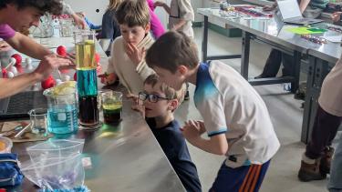 A high school boy and two elementary school boys lean over a counter in a lab during a biology experiment