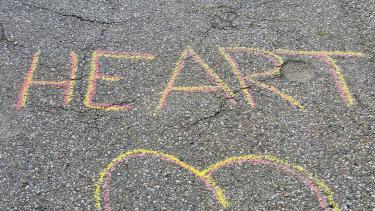 Yellow and pink chalk on pavement that reads, "Run with Heart" and shows a heart drawing below the text