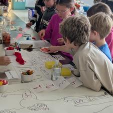 A group of elementary school students lean over a table in a classroom looking at projects displayed there.