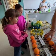 Two girls in pin shirts look at a table with models of how cell membranes work.