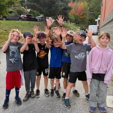 Eight children in shorts, sweatpants, t-shirts and hoodies raise their hands above their head in celebration after finishing a run at a school