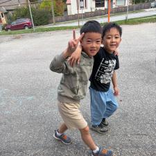 A boy gives a peace sign with his hand while walking with his arm around another boy. They've both just finished a run at a school.