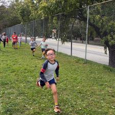 A boy sprints toward the end of a school run across a grassy field on a late summer day