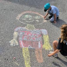 Two children draw a large colourful chalk person on pavement